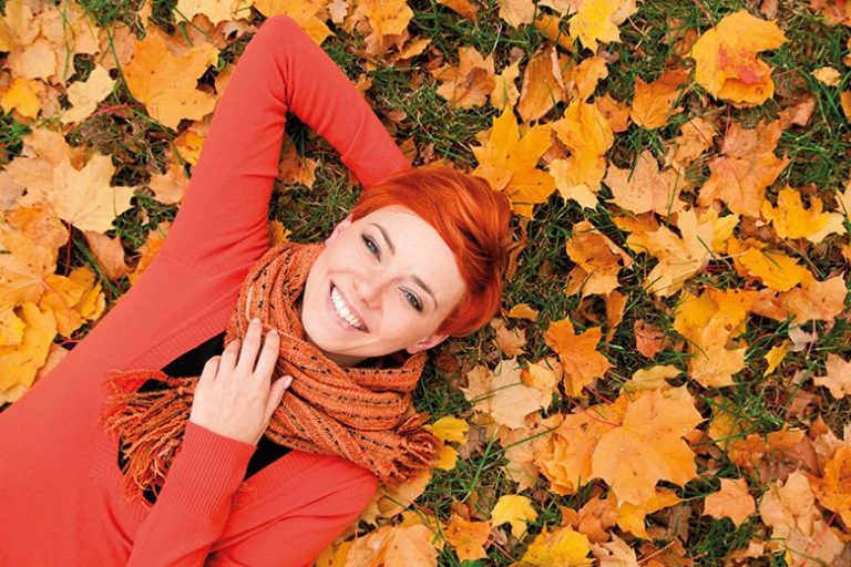 Ragazza dai capelli rossi sorride su un letto di foglie in autunno